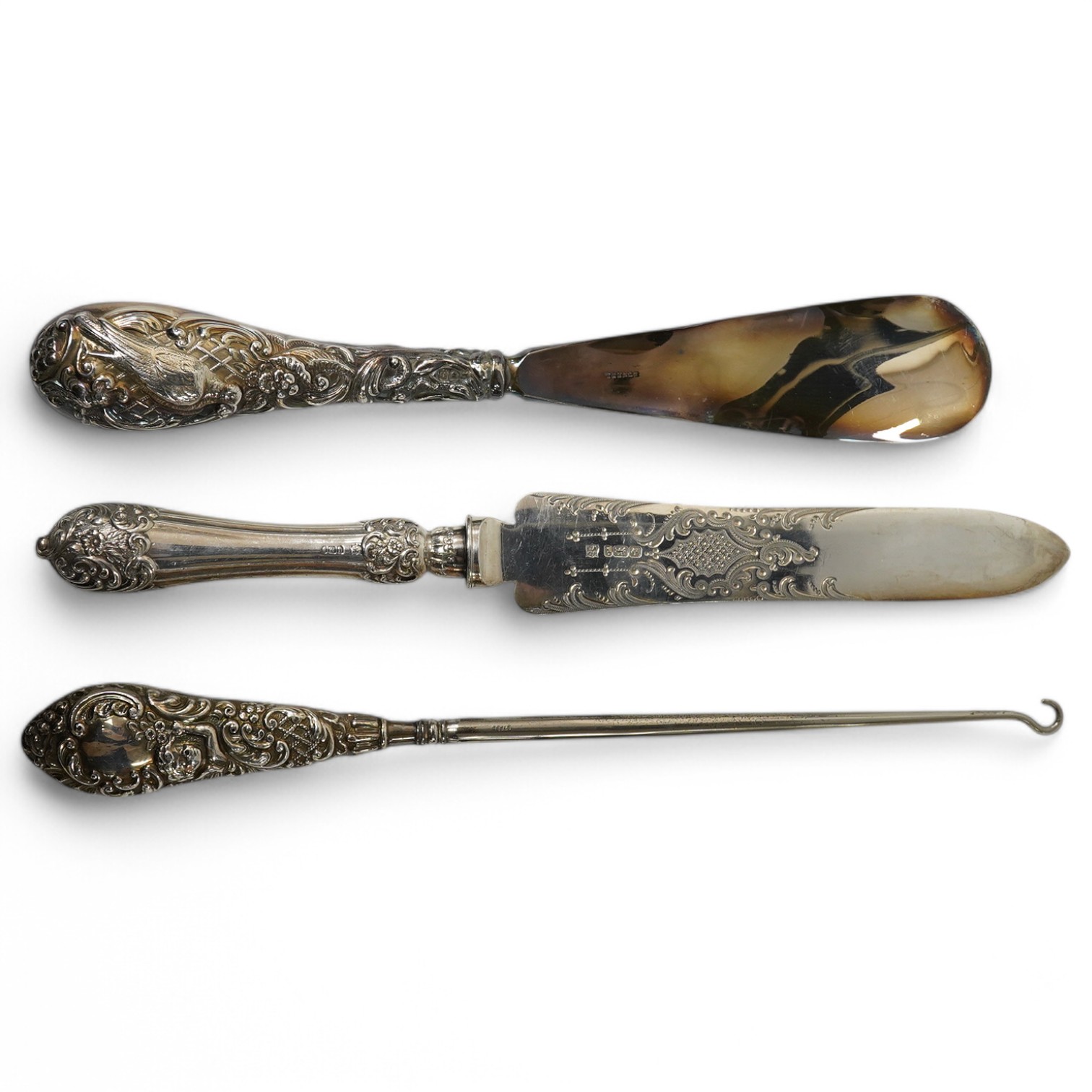 An Edwardian silver cake knife with engraved blade and decorative handle, James Deakin & Sons, Sheffield, 1901, together with a late Victorian silver handled button hook and silver handled shoe horn. Condition - poor to